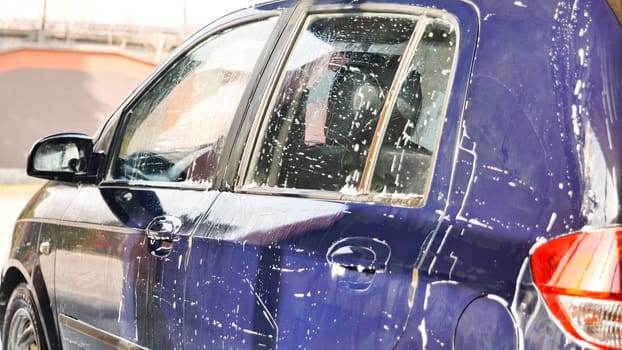 Car wash worker covering a blue car with soap during cleaning service