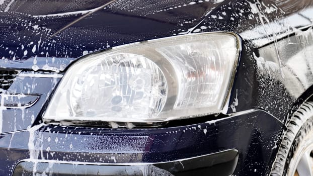 A close-up of a car headlight during a car wash