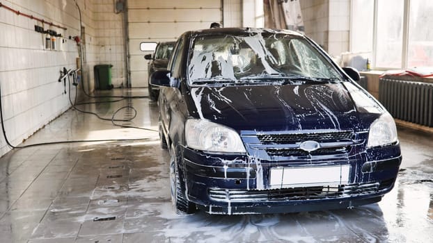 Car covered by soap during washing process in professional car wash station