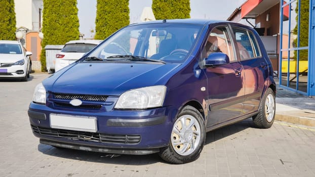 Shiny blue Hyundai Getz parked near a car wash, reflecting the surrounding environment, ready for a thorough cleaning