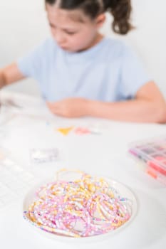 Little girl enjoys crafting colorful bracelets with vibrant clay beads set.