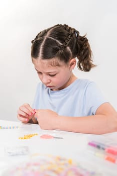 Little girl enjoys crafting colorful bracelets with vibrant clay beads set.