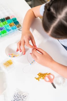 Little girl enjoys crafting colorful bracelets with vibrant clay beads set.