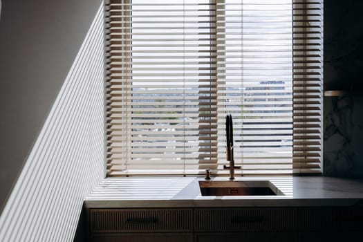 This is a cozy and functional kitchen that features both a sink for washing dishes and a window adorned with blinds for privacy