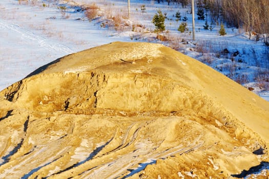 Sand mound rises prominently against a backdrop of snow-covered ground and sparse trees.