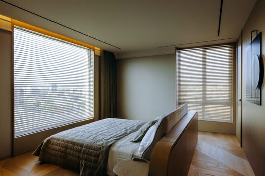 A spacious bedroom featuring a large, comfortable bed complemented by numerous windows that allow natural light to pour in, creating a bright atmosphere