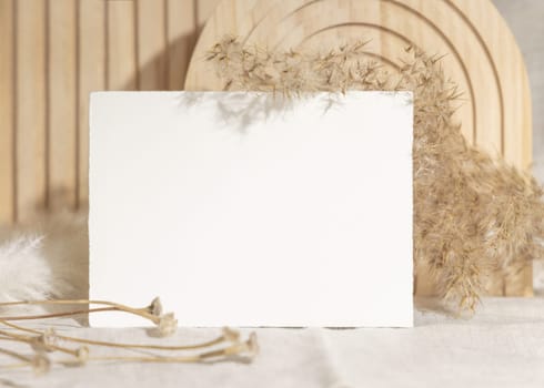 Blank card near dry pampas grass and beige wooden decor on linen closeup, minimal mockup. Boho scene with horizontal card, Bohemian or close to nature wedding stationery or party design