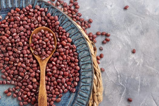 Ceramic blue plate full of dried red azuki beans with a wooden spoon on grey table top view, copy space. Healthy vegetarian food, legumes protein source. Traditional East Asian cousin ingredient