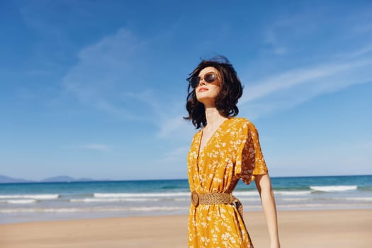 Woman in a vibrant yellow dress standing on sandy beach with scenic ocean view in background