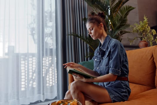 Cozy woman sitting on orange couch with book and bowl of food in living room setting