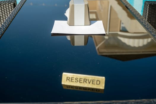 A simple "reserved" sign on a dark table in a poolside restaurant. A box of napkins and a blank sheet of paper are on the table