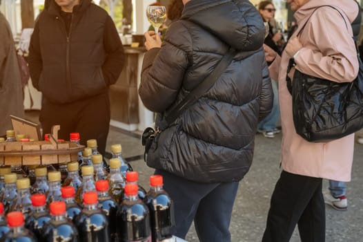 Odessa, Ukraine - April 05, 2025: City food festival, people walking around the market and tasting wine. Women with glasses of vmna in their hands. in the foreground are plastic bottles of wine or juice