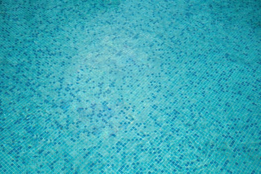 Crystal-clear water rippling over blue mosaic tiles in swimming pool. swimming pool pattern from top. pool water under the sunlight with blue mosaic, swimming pool surface.