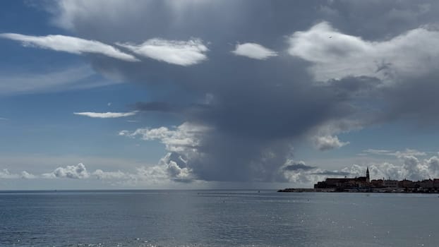 A coastal landscape with dramatic clouds over calm waters that reflect the old town, highlighting the beauty and serenity of nature
