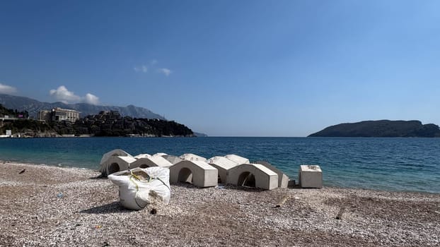 Budva, Montenegro - April 17, 2025: Coastal landscape with stone details for fortification on the beach and a torn bag with pebbles inside