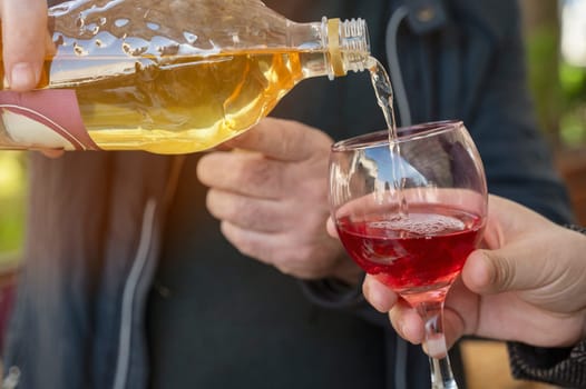 Close-up of hands pouring wine from bottle into glass. The process of mixing yellow and red drink.