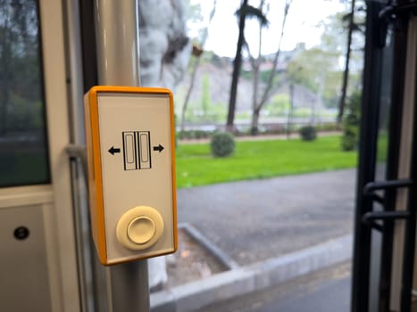 Door open button inside modern public transport, featuring clear sliding door icon and accessible design. Urban background visible through open doors enhances the city mobility context