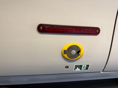 Emergency door release mechanism in public transport vehicle, featuring a sealed handle and clear instruction icon for safe and fast evacuation procedures