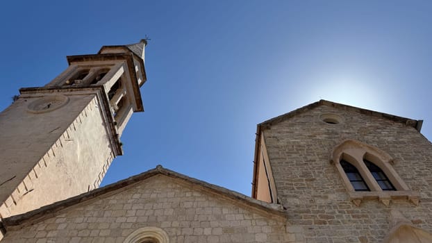 Budva, Montenegro - April 20, 2025: Historic Church of St. John the Baptist with a bell tower under a clear blue sky
