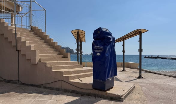 Budva, Montenegro - April 17, 2025:An ATM, covered with a cover for the winter period, stands on the embankment near a cafe