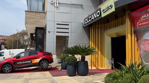 Budva, Montenegro - April 18, 2025: A red Toyota sports car with Volcano branding is displayed on a platform outside a modern casino entrance with bright yellow accents.