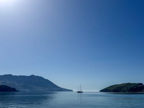 Budva, Montenegro - April 18, 2025: A calm seascape with a sailboat and mountains under a clear blue sky evokes a sense of serenity and peace in nature