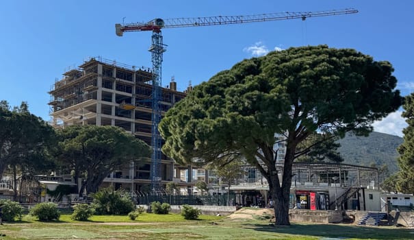 Budva, Montenegro - April 18, 2025: The urban development project highlights Swissotel's construction site showcasing a crane lifting materials alongside natural elements, highlighting the harmony between progress and nature