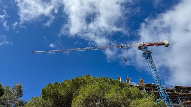 Budva, Montenegro - April 18, 2025: A construction crane towers over the Swissotel construction site against a backdrop of blue skies and clouds, symbolizing urban development and progress