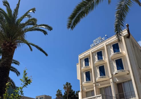 Budva, Montenegro - April 18, 2025: Hotel Mogren stands prominently against a clear blue sky, surrounded by palm trees, evoking a tropical vacation atmosphere