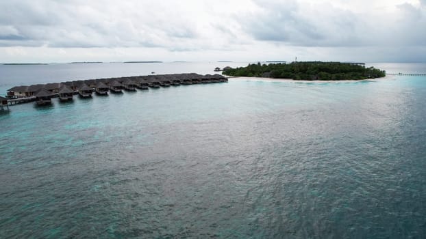 Stunning aerial view of a row of overwater bungalows in the maldives, showcasing the beauty of luxury travel and tropical paradise, with a cloudy sky adding a touch of drama