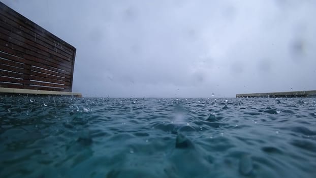 Rain falling on a turquoise swimming pool during a cloudy day creates mesmerizing ripples and splashes on the water's surface, enhancing the tranquil atmosphere of the scene