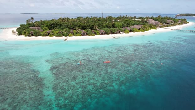 Tourists enjoy kayaking and paddleboarding in the crystal-clear turquoise waters surrounding a tropical island resort in the maldives, showcasing the vibrant coral reef below