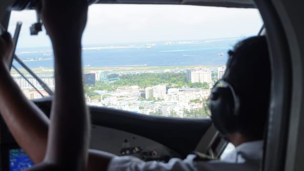 Two pilots are flying a seaplane over male, capital of maldives, approaching the airport, with the ocean and several boats visible in the background