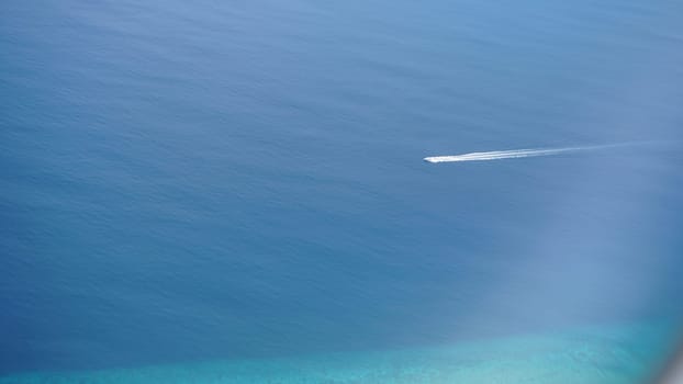 Speedboat gliding across deep blue waters, leaving a striking white trail behind. Aerial view captures the small boat navigating the ocean above a vibrant turquoise seabed