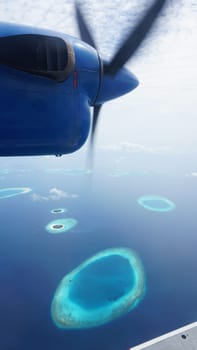 Atolls of maldives archipelago in the indian ocean seen from airplane window with part of aircraft and spinning propeller, luxury travel destination