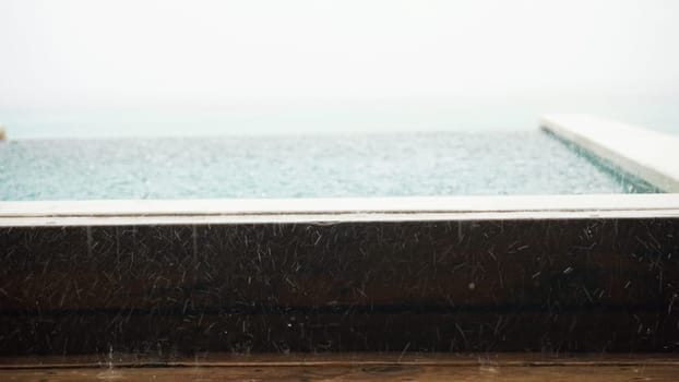 Rain cascading on an infinity pool overlooking the ocean creates a serene and moody atmosphere during a stormy day, enhancing the tranquil beauty of the seascape