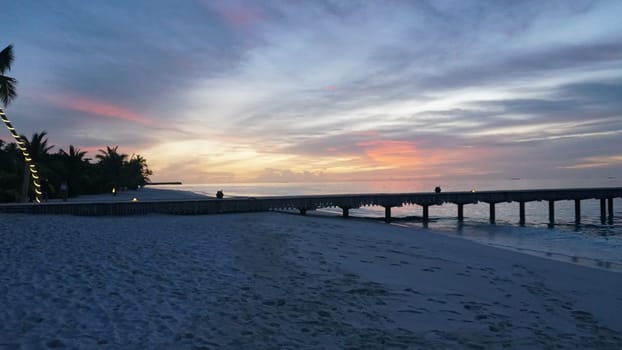 Tranquil scene of a wooden pier extending into the ocean under a vibrant sunset sky in the maldives, capturing the serene beauty of the tropical paradise