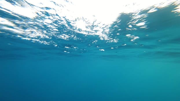 Underwater view of the ocean surface with sun rays shining through the waves, creating a beautiful and serene atmosphere, perfect for backgrounds and nature-themed projects