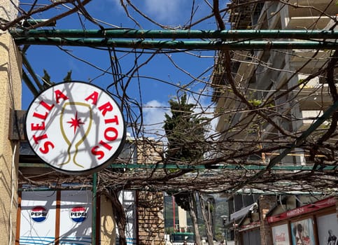 Budva, Montenegro - April 18, 2025: Stella Artois sign in an urban environment, surrounded by vines and bright blue skies, reflecting the local culture and public spirit
