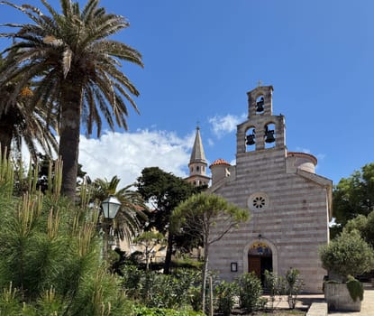 Budva, Montenegro - April 20, 2025, a historic Church of the Holy Trinity in the Old Town, surrounded by palm trees and lush greenery.