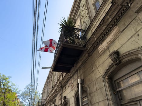 Close up of decaying classical building facade with cracked paint and vintage balcony. Old European architecture detail with character and texture, under clear sky and visible utility lines
