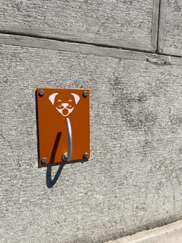 Minimalist plate with smiling dog icon and metal hook on raw concrete wall. Functional street element with strong visual identity designed for simplicity and intuitive use