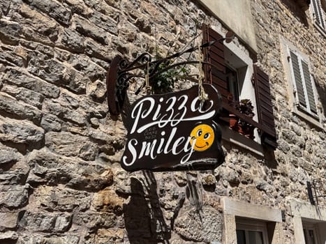 Budva, Montenegro - April 18, 2025: Pizza Smiley sign on a rustic stone wall in the Old Town. inviting joy and a sense of community through its fun design