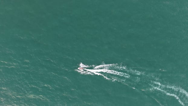 Aerial view of a personal watercraft creating a wake on a beautiful turquoise ocean surface, capturing the thrill and freedom of water sports