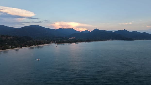 Tranquil coastal scenery featuring calm waters, lush mountains, and a vibrant sunset sky. The peaceful shoreline invites relaxation and contemplation, highlighting nature's beauty