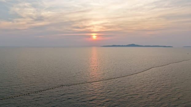 Golden hues of sunset paint the sky over a tranquil ocean, its surface reflecting the light as distant islands silhouette against the horizon, creating a serene and picturesque seascape