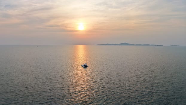 Golden sun setting over a tranquil ocean, casting a warm glow on the water as a catamaran sails peacefully towards the horizon, with a distant island adding to the serene seascape