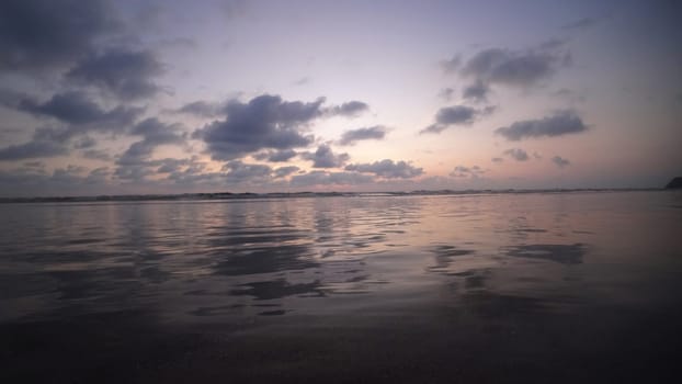 Calm ocean waves reflecting golden sunset light dance beneath a stunning cloudy sky, creating a tranquil and serene atmosphere perfect for evening relaxation