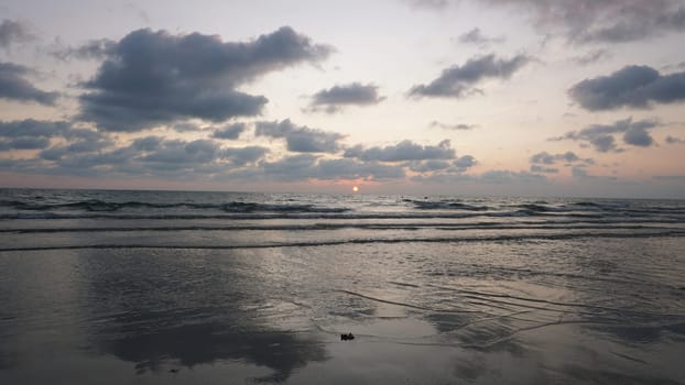 Soft waves gently roll onto the sandy shore as the sun dips below the horizon, painting the sky with vibrant hues of orange and pink during a serene sunset at the beach