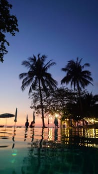 Palm trees swaying gently in the breeze as tourists relax in an infinity pool, taking in the breathtaking view of a vibrant sunset over a tropical ocean